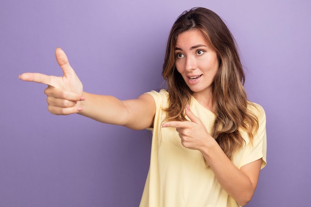 Jonge mooie vrouw in beige t-shirt die opzij kijkt glimlachend wijzend met wijsvingers naar de zijkant