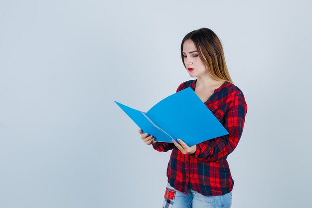 Jonge mooie vrouw in casual shirt, jeans die naar de map kijkt en er somber uitziet, vooraanzicht.