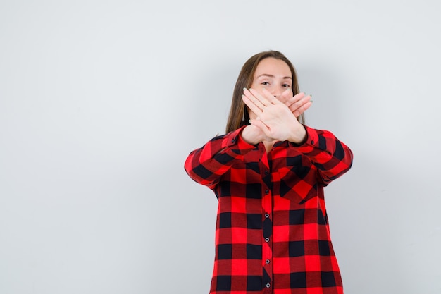 Jonge mooie vrouw in casual shirt met stopgebaar met gekruiste handen en zelfverzekerd, vooraanzicht.