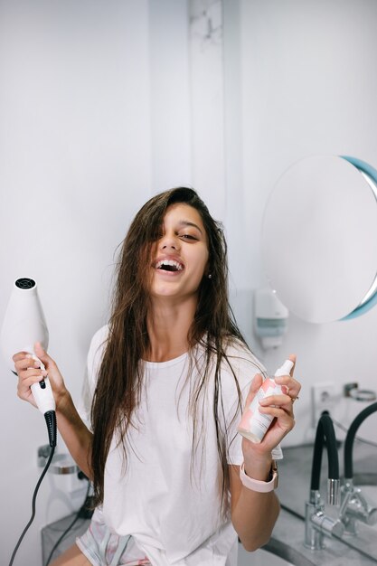 Jonge mooie vrouw in de badkamer met een haardroger en een kleine fles, dichtbij bekeken