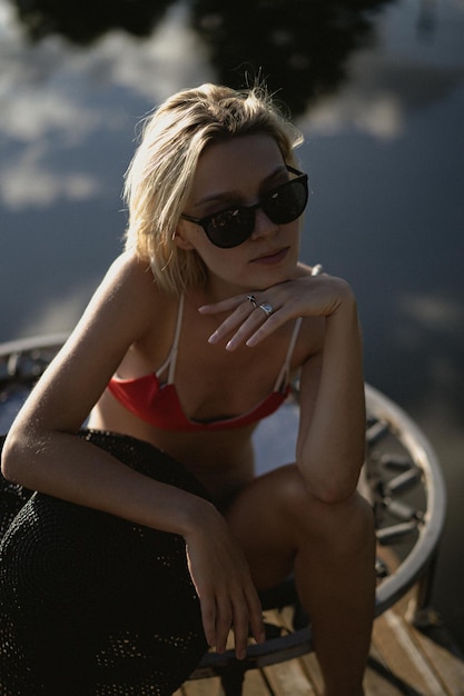 jonge mooie vrouw in een zwarte strohoed en rode zwembroek, zonnebril zonnebaden op een ligstoel, het concept van openluchtrecreatie.