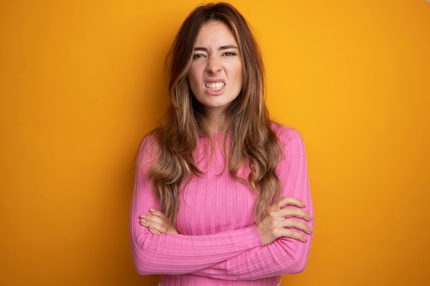 Jonge, mooie vrouw in roze top die naar de camera kijkt met een boos gezicht over een oranje achtergrond