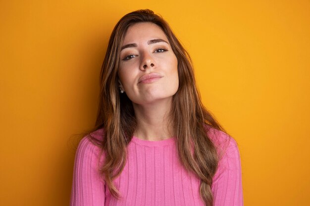 Jonge mooie vrouw in roze top die naar de camera kijkt met een zelfverzekerde uitdrukking die over oranje staat