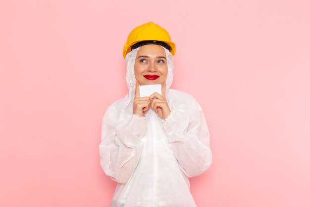 Jonge mooie vrouw in speciaal wit pak en gele helm met witte kaart op roze