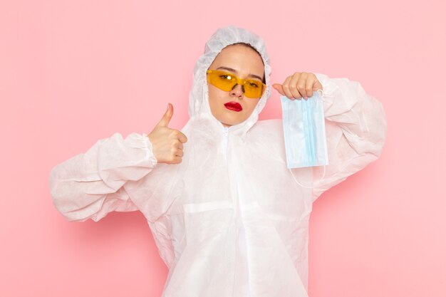 Gratis foto jonge mooie vrouw in speciaal wit pak steriel beschermend masker op roze te houden