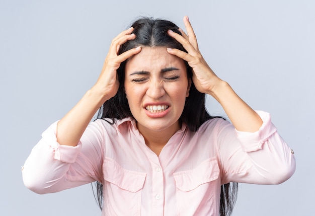 Jonge mooie vrouw in vrijetijdskleding die haar haar trekt met een teleurgestelde uitdrukking die over een witte muur staat