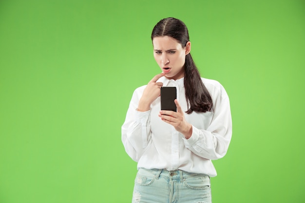 Jonge mooie vrouw met behulp van mobiele telefoon in de studio op groene kleur achtergrond. menselijke gezichtsemoties concept.