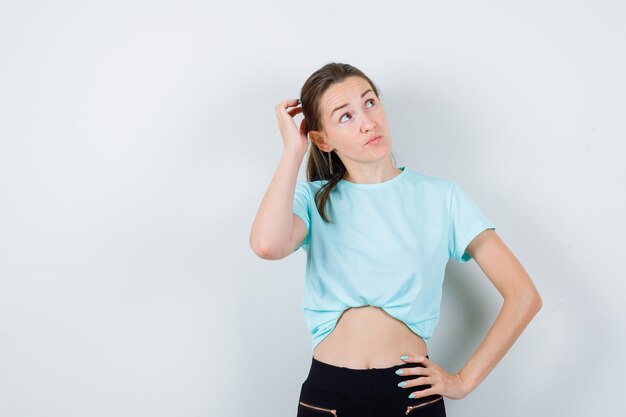 Jonge mooie vrouw met de hand op het hoofd, wegkijkend in t-shirt en peinzend kijkend. vooraanzicht.