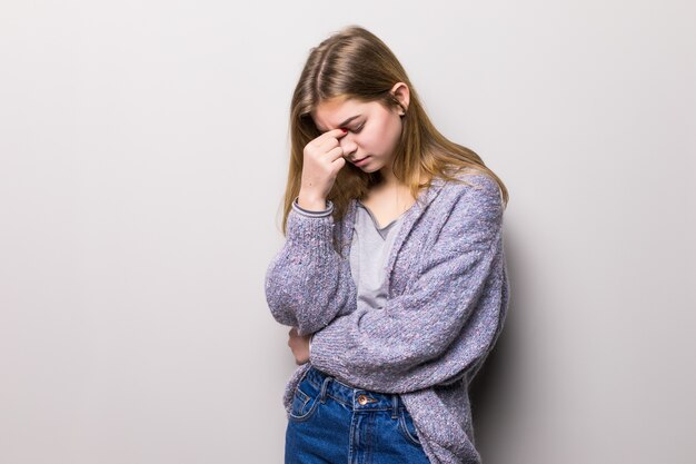 Jonge mooie vrouw met hoofdpijn die op grijze muur wordt geïsoleerd.