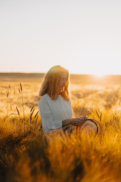 jonge mooie vrouw met lang blond haar in een witte jurk op een tarweveld in de vroege ochtend bij zonsopgang. De zomer is de tijd voor dromers, vliegend haar, een vrouw die in de stralen over het veld rent