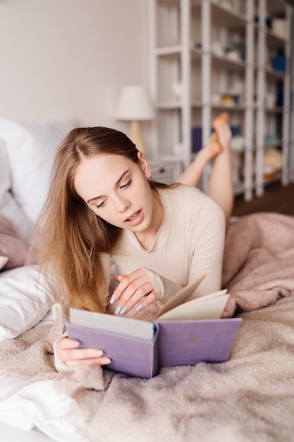 Jonge mooie vrouw op bed thuis genieten van favoriete boek