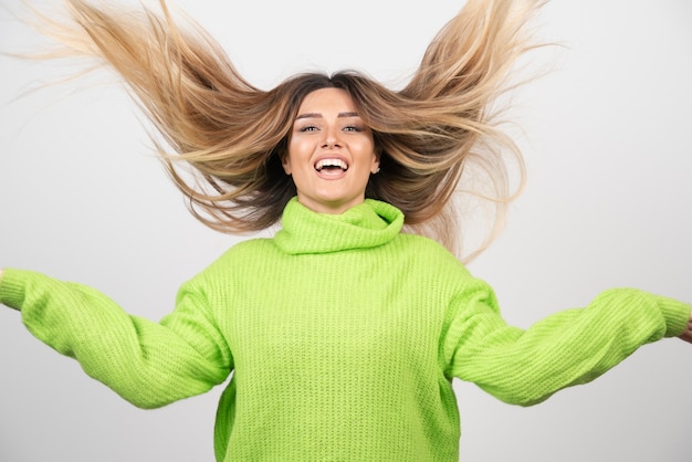 Gratis foto jonge mooie vrouw poseren in groene trui over een witte muur.