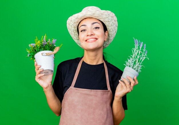 Jonge mooie vrouw tuinman in schort en hoed met potplanten lachend met blij gezicht