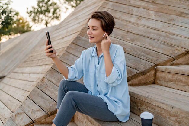 Jonge mooie vrouw zit met laptop in moderne parkstraat met smartphone