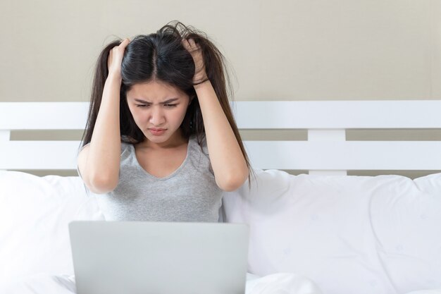 Jonge mooie vrouw zittend op bed, ze gebruikt laptop en voel me serieus en helaas