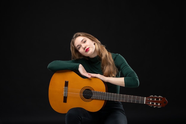 Jonge mooie vrouwelijke gitarist die haar favoriete muziekinstrument op dark houdt