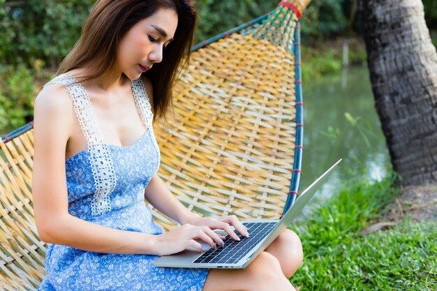 Jonge mooie vrouwenzitting in bamboehangmat die laptop met behulp van
