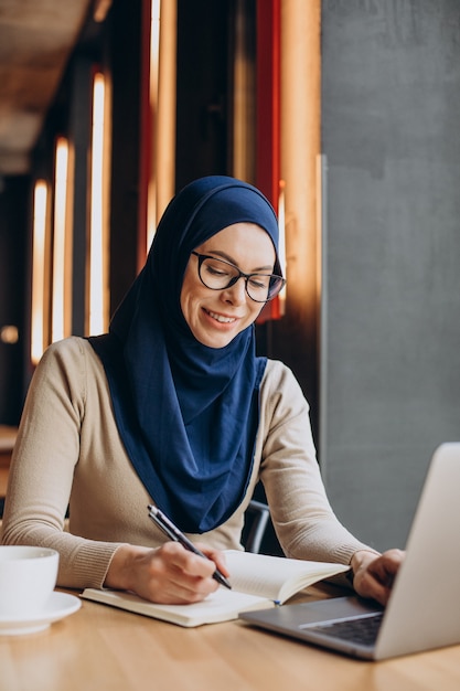 Jonge moslimvrouw die online werkt op de computer in een café