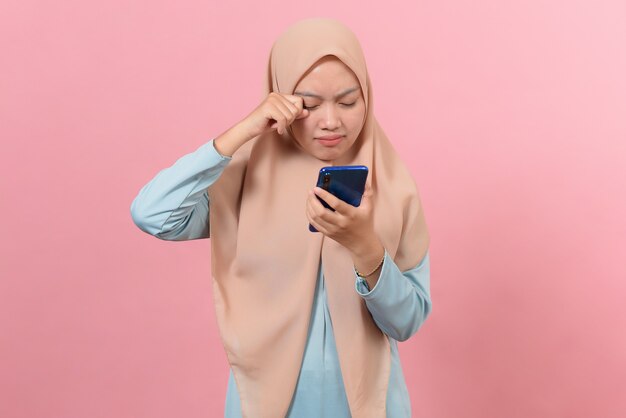 Jonge moslimvrouw huilen kijken naar smartphone geïsoleerd op roze achtergrond