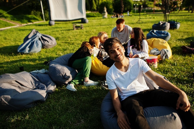 Jonge multi-etnische groep mensen kijken naar film op poef in openluchtbioscoop Close-up portret van grappige kerel