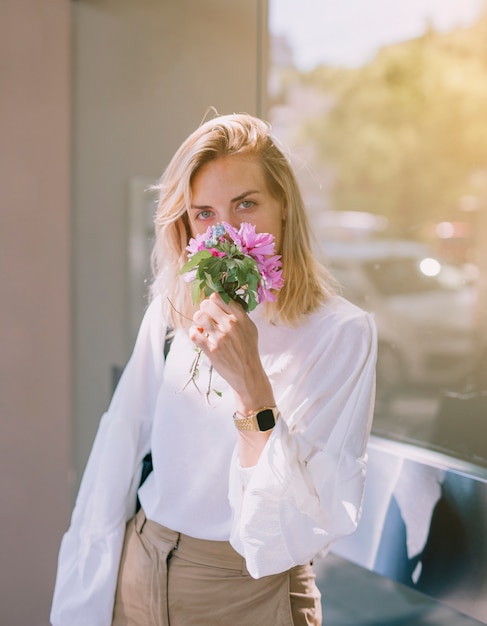 Jonge onderneemster die de bloemen ruikt die in hand houden en aan camera kijken