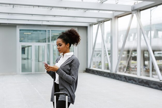 Jonge onderneemster die in luchthaventerminal wacht die mobiele telefoon controleert