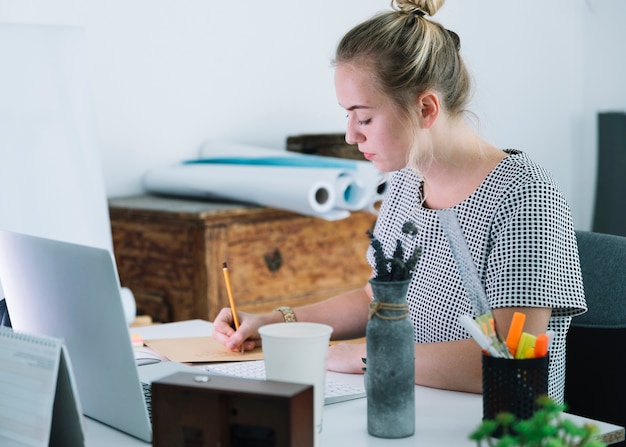 Jonge onderneemster die op papier over het bureau schrijft