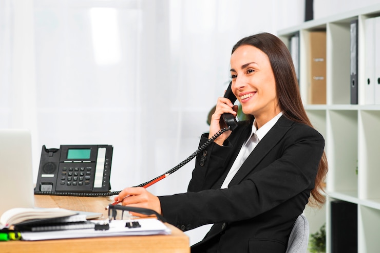 Gratis Foto jonge onderneemster die terwijl het spreken op telefoon in het bureau glimlacht