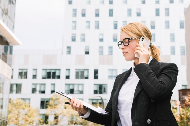 Jonge onderneemster die zich buiten de collectieve gebouwen bevindt die op mobiele telefoon spreken