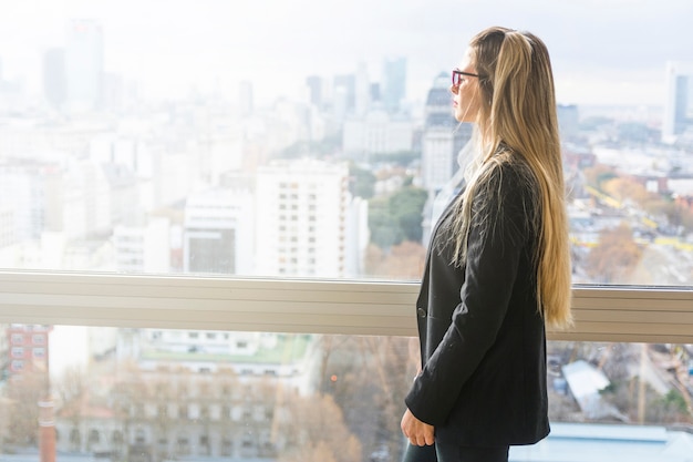 Jonge onderneemster die zich dichtbij het vensterglas in het bureau bevindt