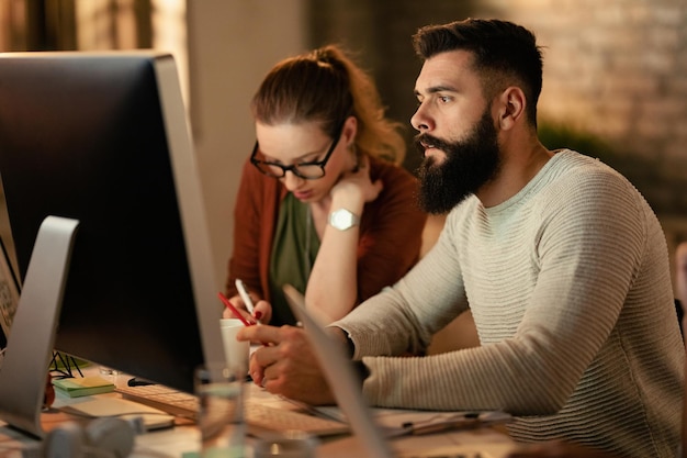 Gratis foto jonge ondernemer die computer gebruikt terwijl hij met zijn collega's op kantoor werkt