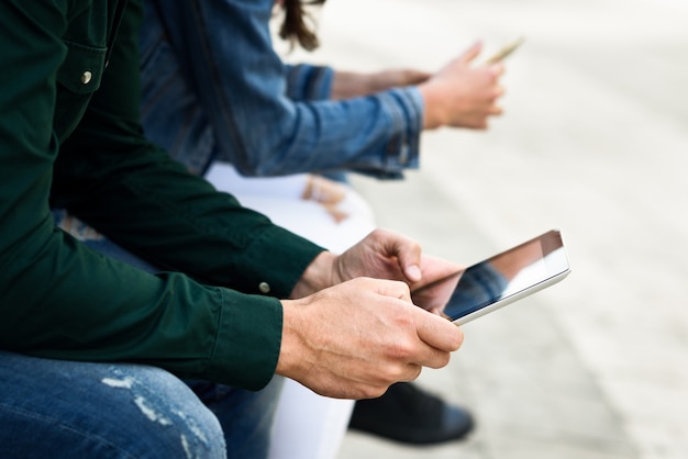 Jonge onherkenbare mensen die smartphone en tabletcomputer gebruiken