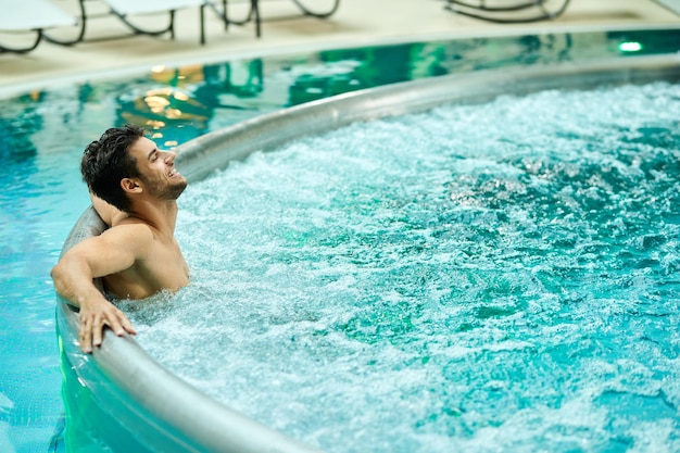 Jonge ontspannen man die geniet in een bubbelbad terwijl hij een dag doorbrengt in het wellnesscentrum