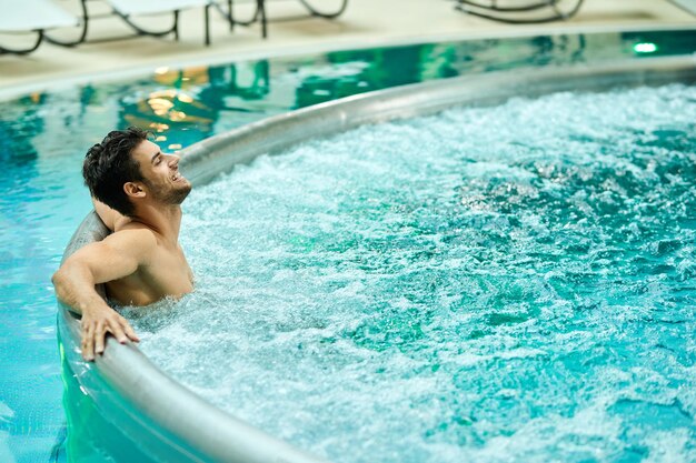 Jonge ontspannen man die geniet in een bubbelbad terwijl hij een dag doorbrengt in het wellnesscentrum