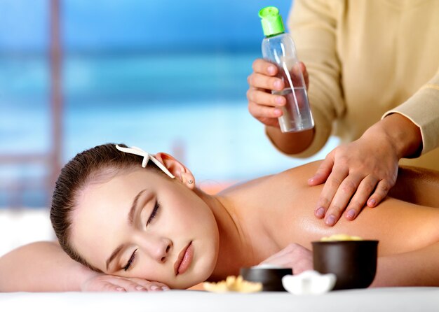 Jonge ontspannende mooie vrouw die massage met kosmetische olie krijgt in kuuroordsalon