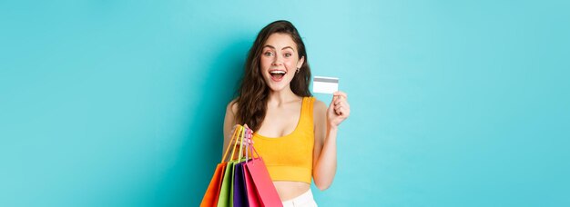 Jonge opgewonden vrouw die boodschappentassen vasthoudt en plastic creditcard laat zien die dingen koopt tijdens promo