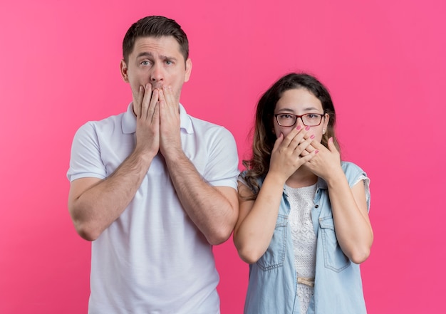 Jonge paarman en vrouw in vrijetijdskleding die mond behandelen met handen die over roze worden geschokt