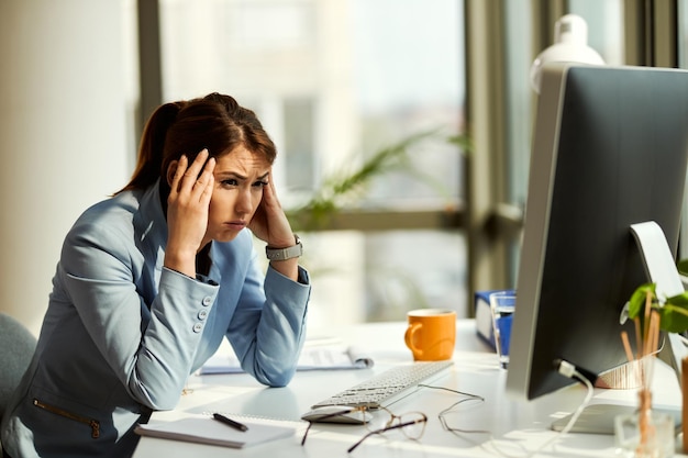 Jonge peinzende zakenvrouw die hoofdpijn heeft terwijl ze problemen heeft op het werk