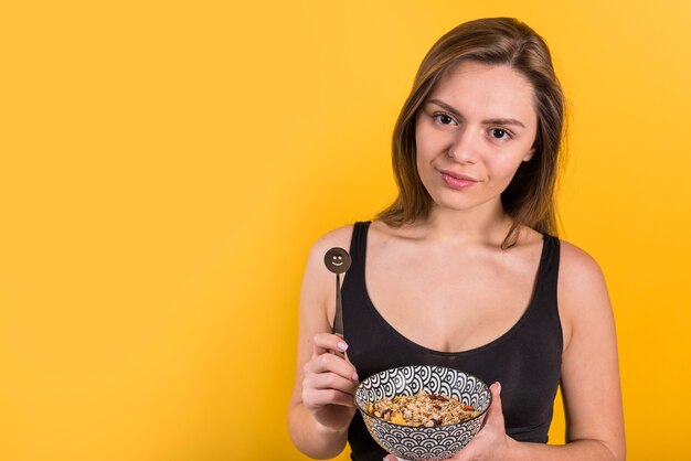 Jonge positieve vrouw met chocoladelepel en kom vlokken