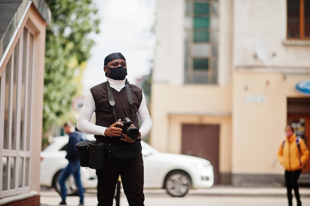 Jonge professionele afro-amerikaanse videograaf met professionele camera met pro-apparatuur afro-cameraman met zwarte duraq en gezichtsbeschermingsmasker dat video's maakt