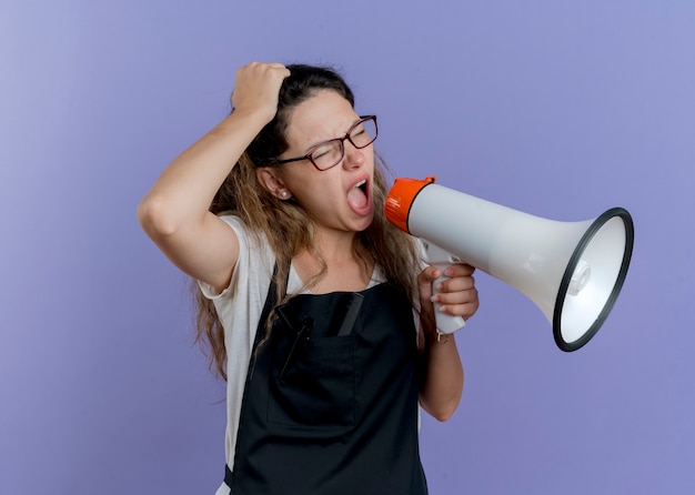 Gratis foto jonge professionele kapper vrouw in schort schreeuwen naar megafoon wordt gefrustreerd