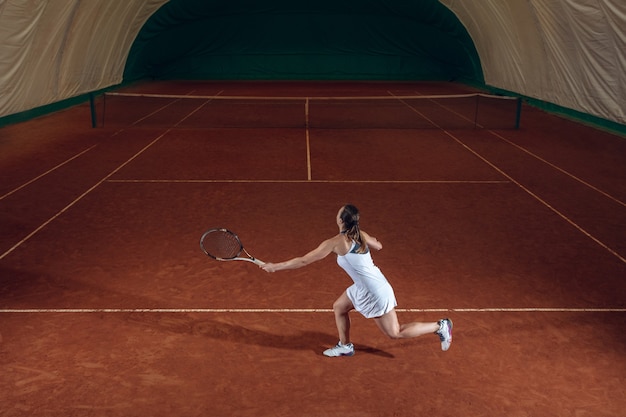 Jonge professionele sportvrouw tennissen op de muur van het sportveld