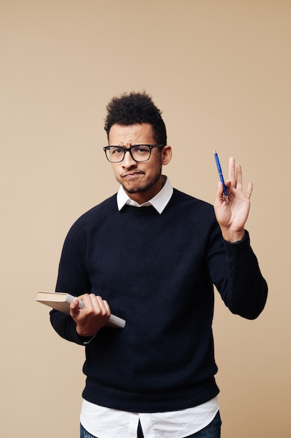 Jonge professor die een boek vasthoudt terwijl hij uitlegt over het dragen van een bril op een beige muur