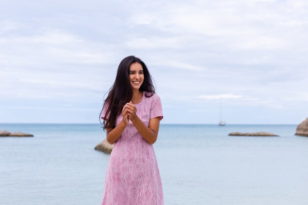 Jonge romantische vrouw met lang donker haar in een jurk op het strand glimlachen en lachen met een leuke tijd alleen