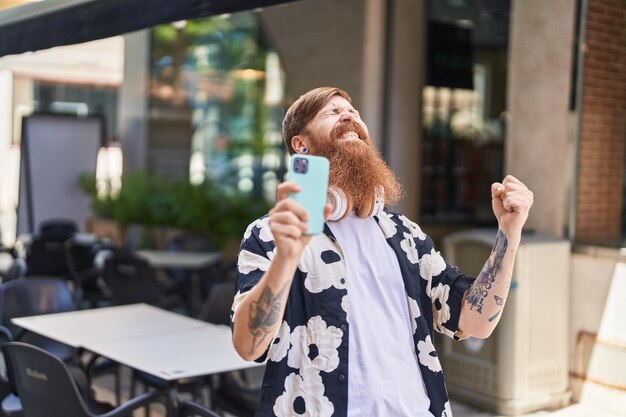 Jonge roodharige man met behulp van smartphone met uitdrukking van de winnaar op straat