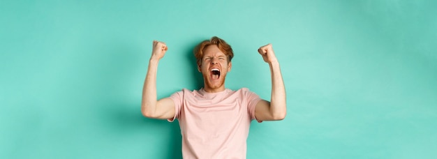 Jonge roodharige man zegeviert terwijl hij naar een sportwedstrijd kijkt en een weddenschap plaatst op het winnende team en zich verheugt over screami