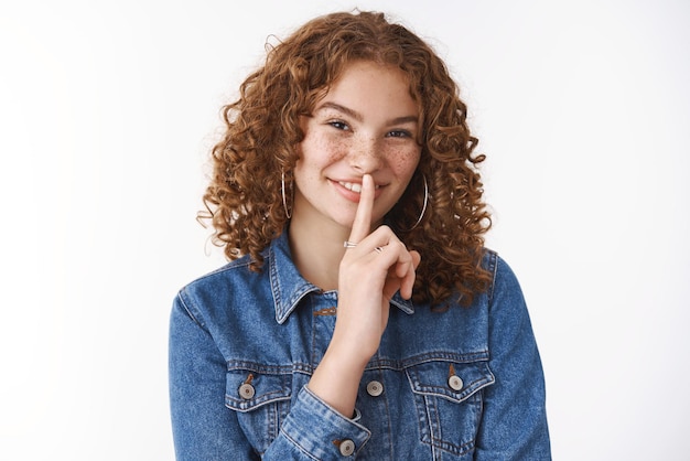 jonge roodharige vrouw met krullend haar laat een shhh-gebaar zien