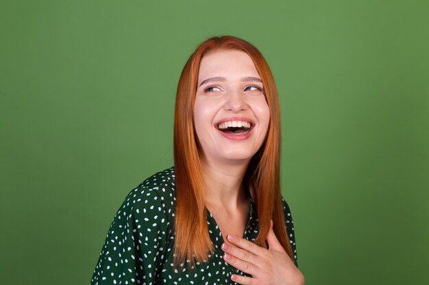 Jonge roodharige vrouw op groene muur lacht en lacht, in een goed humeur, positieve emoties