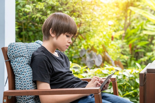 Jonge schattige blanke jongen met behulp van digitale tablet zittend op de bank in de tuin thuis