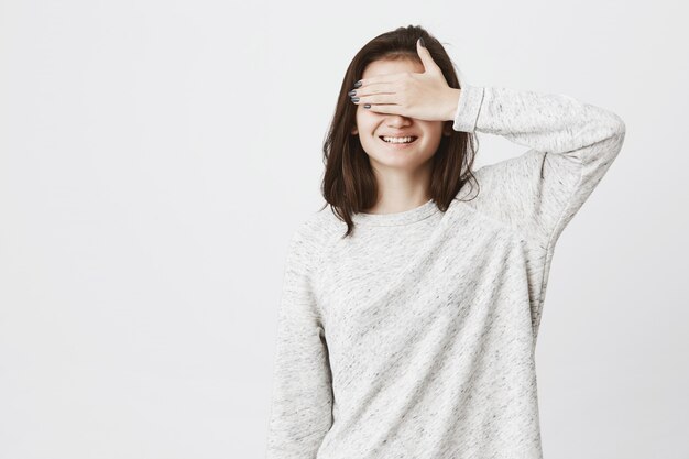 jonge schattige Europese vrouw, die haar ogen met de hand terwijl vrolijk lachend, ongeduldig.